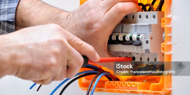 Electrician technician working on a residential electrical panel, fixing with a screwdriver the cable in the magnetothermal switch